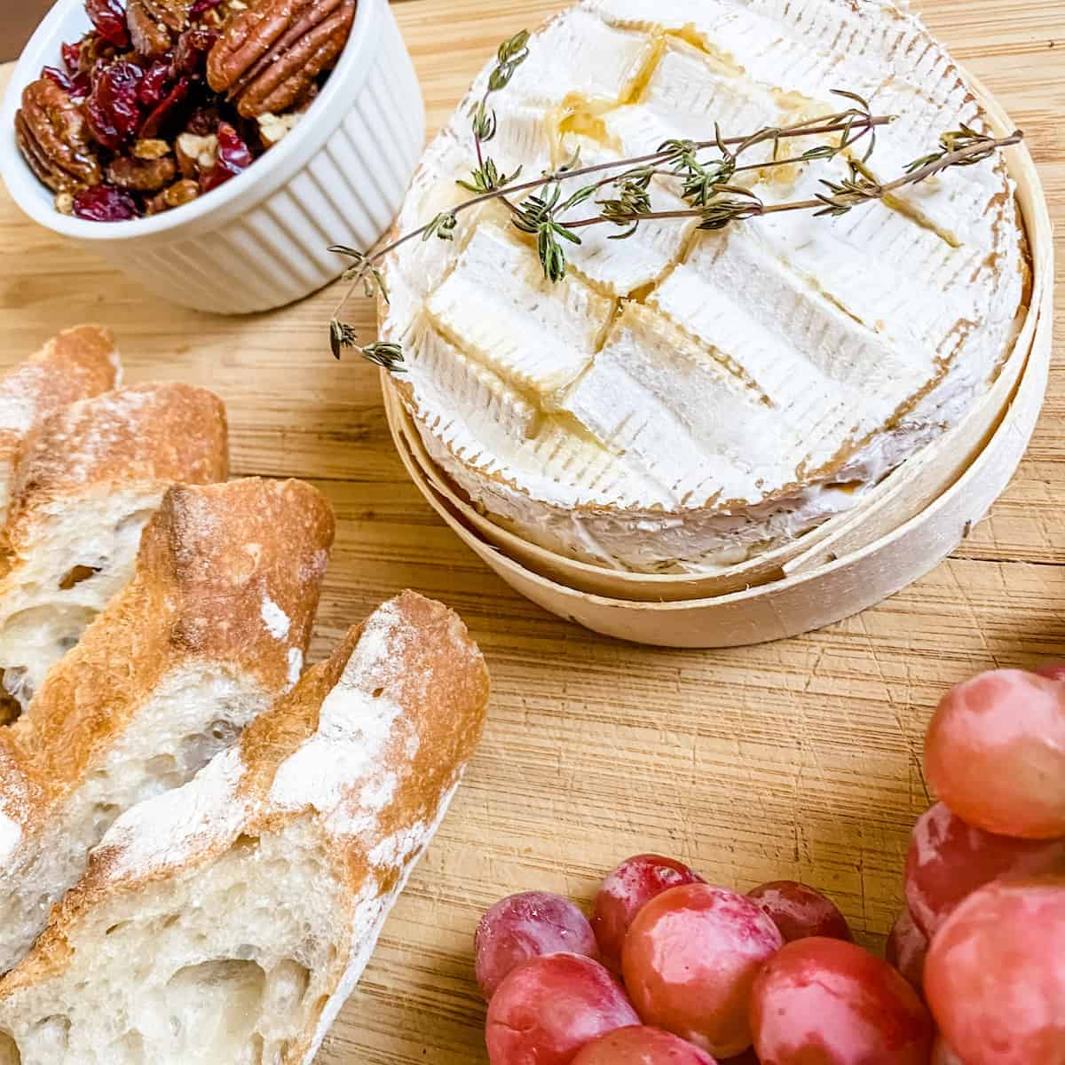 Baked camembert on a wooden serving board with grapes and bread.