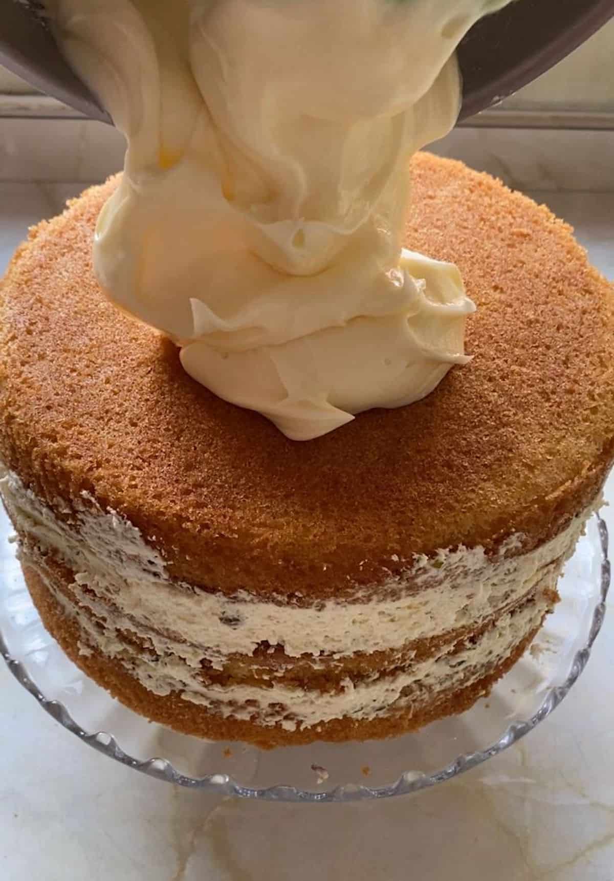 White chocolate buttercream icing being poured on top of a three tiered cake. 