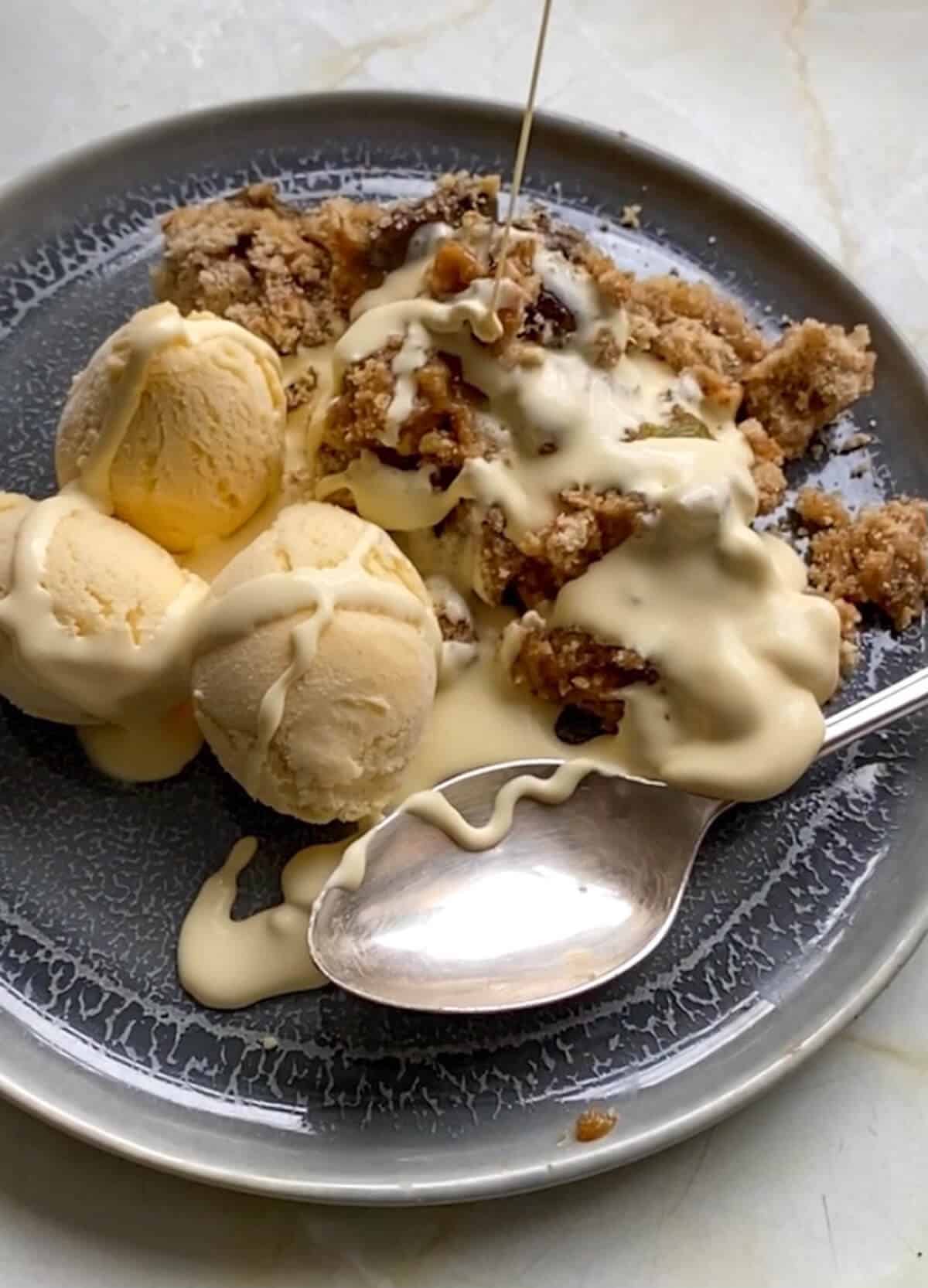 greengage and hazelnut crumble with scoops of vanilla ice cream and cream poured on top