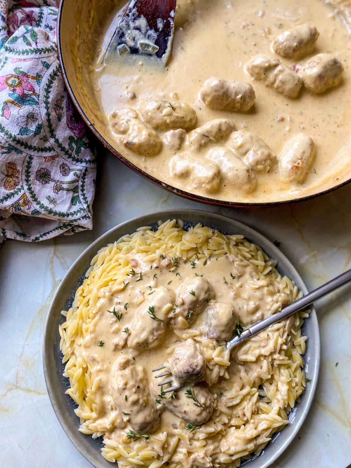 a plate of sausage meatballs cooked in a creamy mustard sauce and served on a bed of orzo pasta 