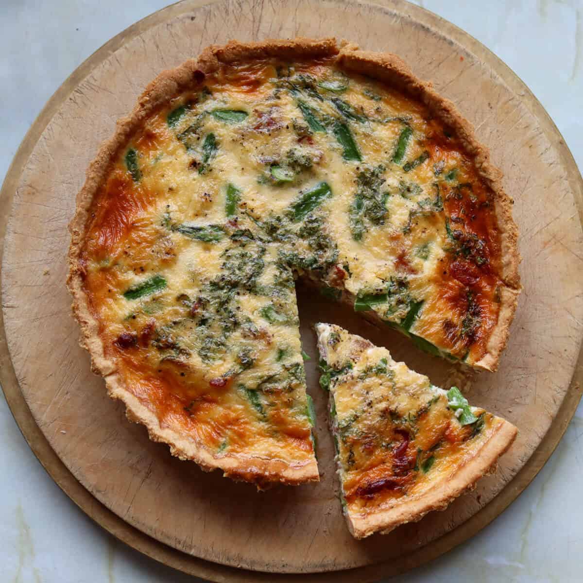 An asparagus and crispy prosciutto quiche on a wooden serving board