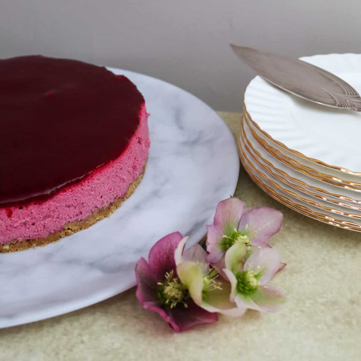 A blackcurrant Mousse Cake with a stack of dessert plates.