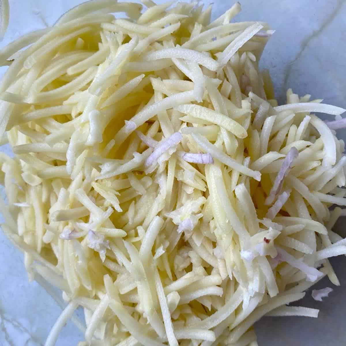 Raw grated potato and shallot in a mixing bowl.