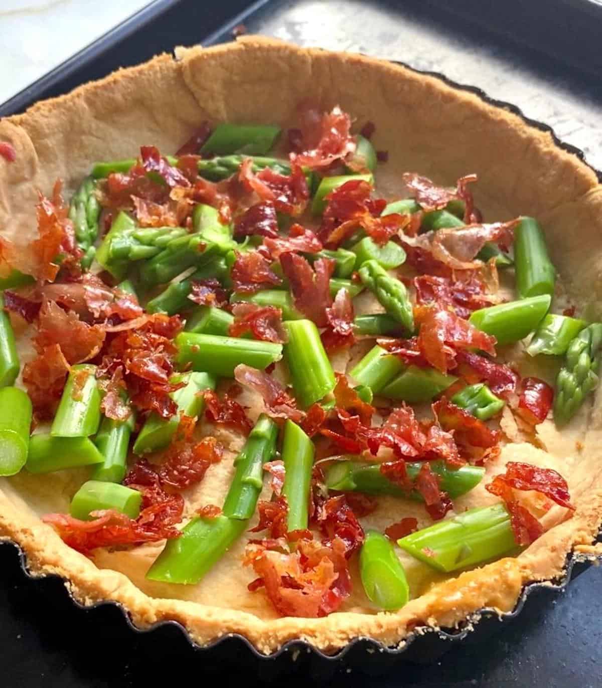 A pastry case half filled with chopped asparagus and crispy prosciutto 