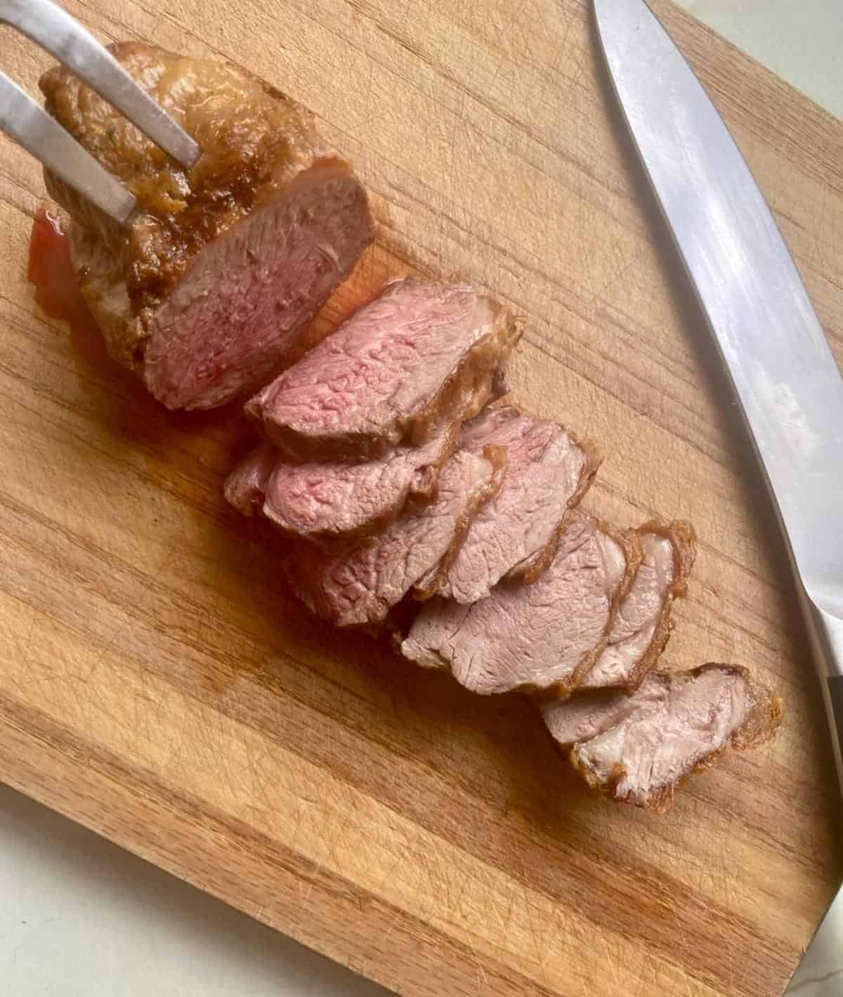 Juicy lamb rump roast being carved on a wooden board