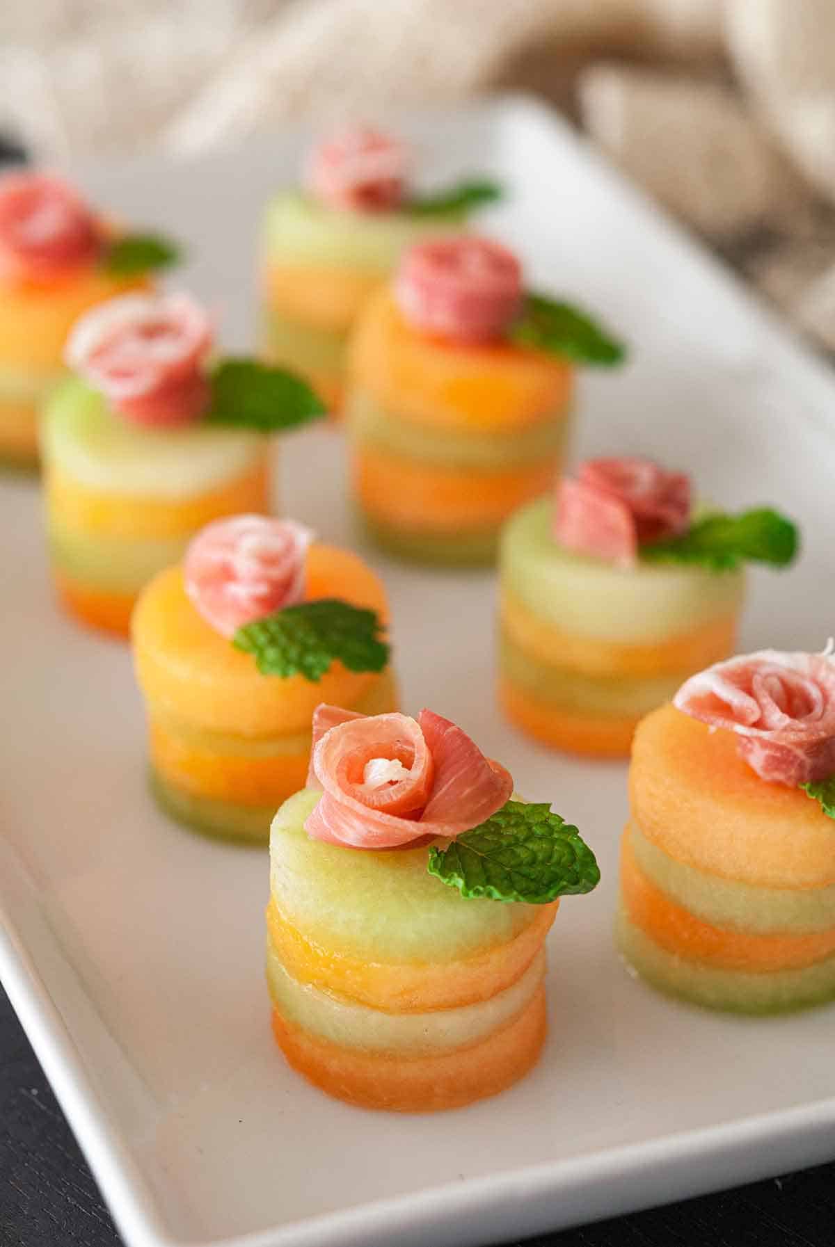 Small and dainty Easter canapés made from stacks of honeydew and cantaloupe melons topped with prosciutto and a mint leaf 