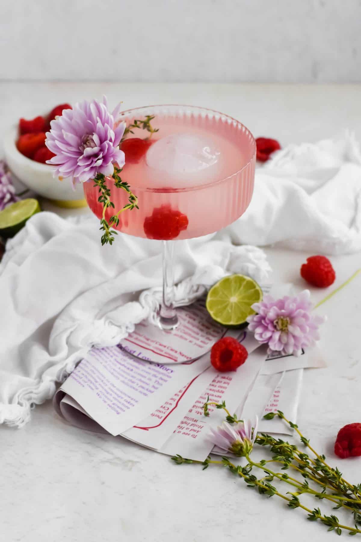 Raspberry Hibiscus Cocktail in a coup glass with flower and berry garnish 