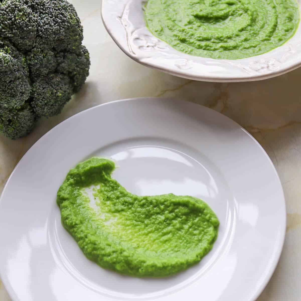 A plate with a smear of truffle broccoli asparagus puree on it and a whole head of broccoli