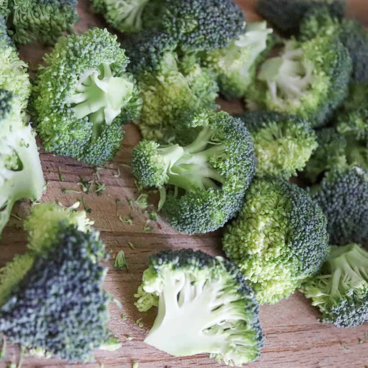 raw broccoli florets with the stalks trimmed to a short length on a wooden chopping board