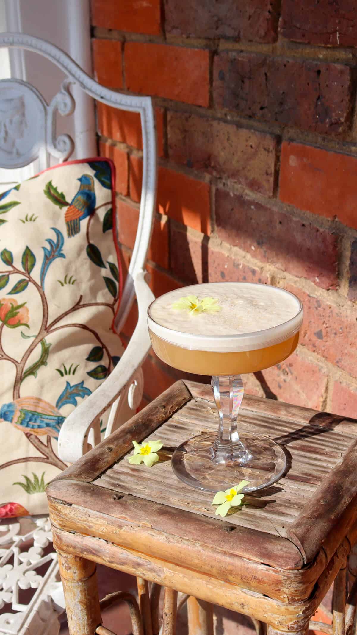 Toasted almond and apricot gin fizz on a small table next to a chair. 