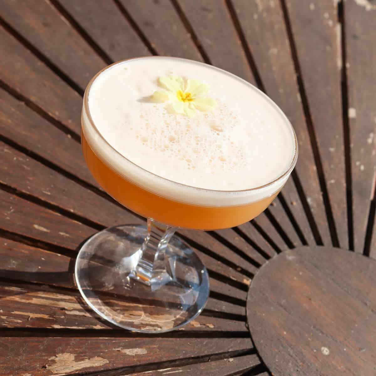 A toasted almond and apricot gin cocktail in a coup glass on a table. 