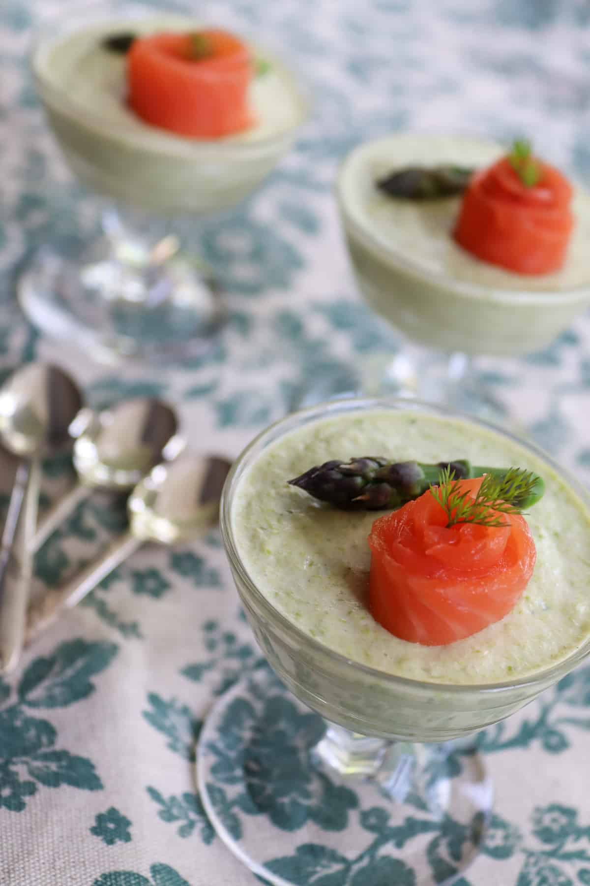 Three small asparagus mousse in serving glasses with smoked trout and fresh asparagus spears on top 