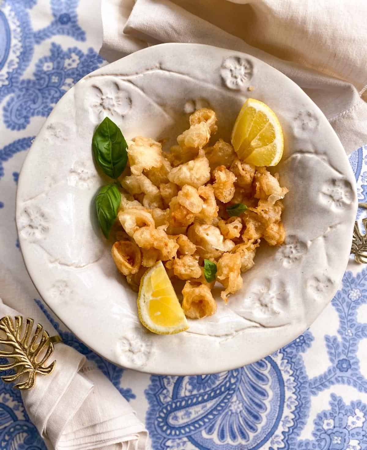 A bowl of popcorn calamari with lemon wedges and fresh basil