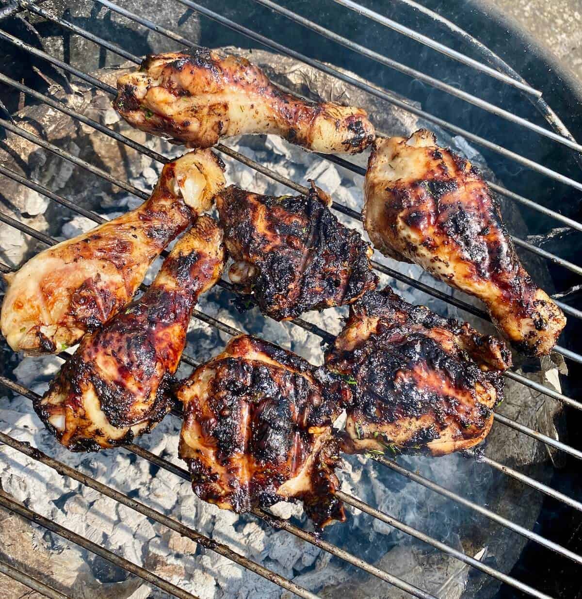 Black garlic chicken thighs and drumsticks cooking on a BBQ grill.