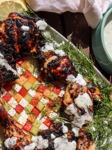A serving of black garlic chicken with a side bowl of feta dill dressing and a melon salad.