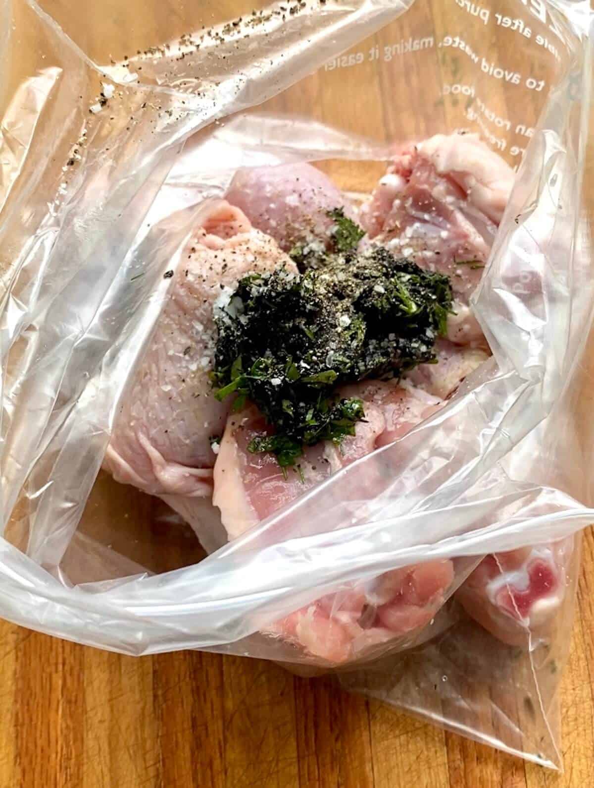 A ziplock bag with raw chicken pieces inside it and the black garlic marinade.