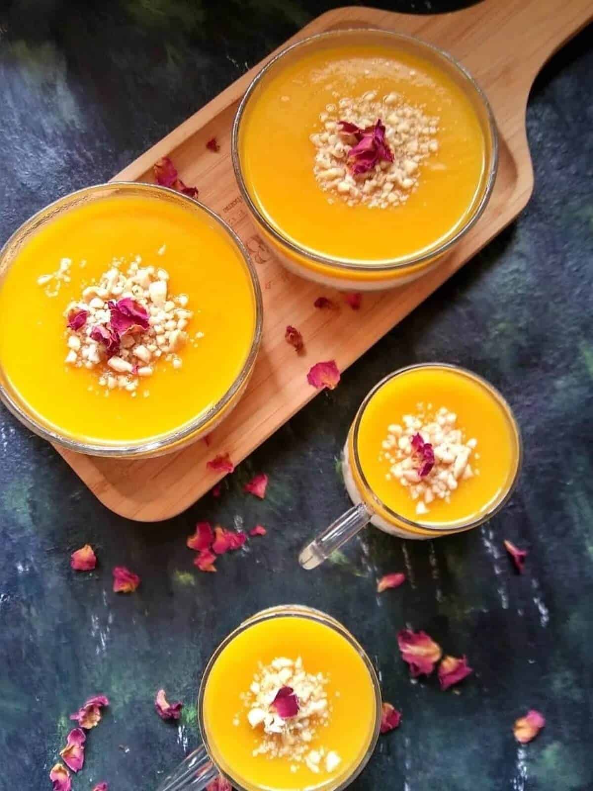 Four glasses of Mango Mahalabia with scattered dried rose petals. 