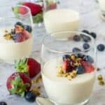 3 drinking glasses filled with panna cotta that is topped with fresh berries and pistachio nuts