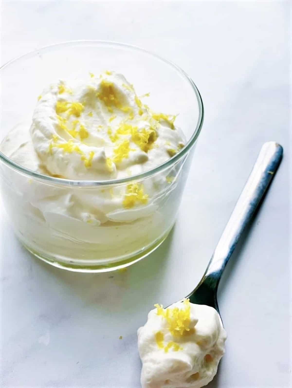 A glass full of lemon syllabub and a dessert spoon.