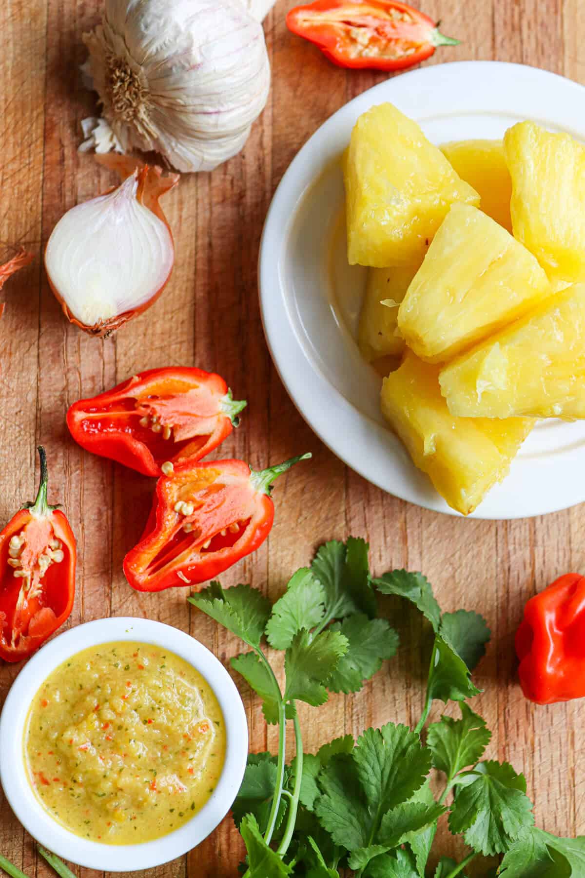 Ingredients for pineapple hot sauce laid out on a chopping board. Image shows pineapple, shallot, coriander, garlic, habanero chillis and lime. 