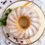 An almond bundt cake on a cake stand, dusted with icing sugar.