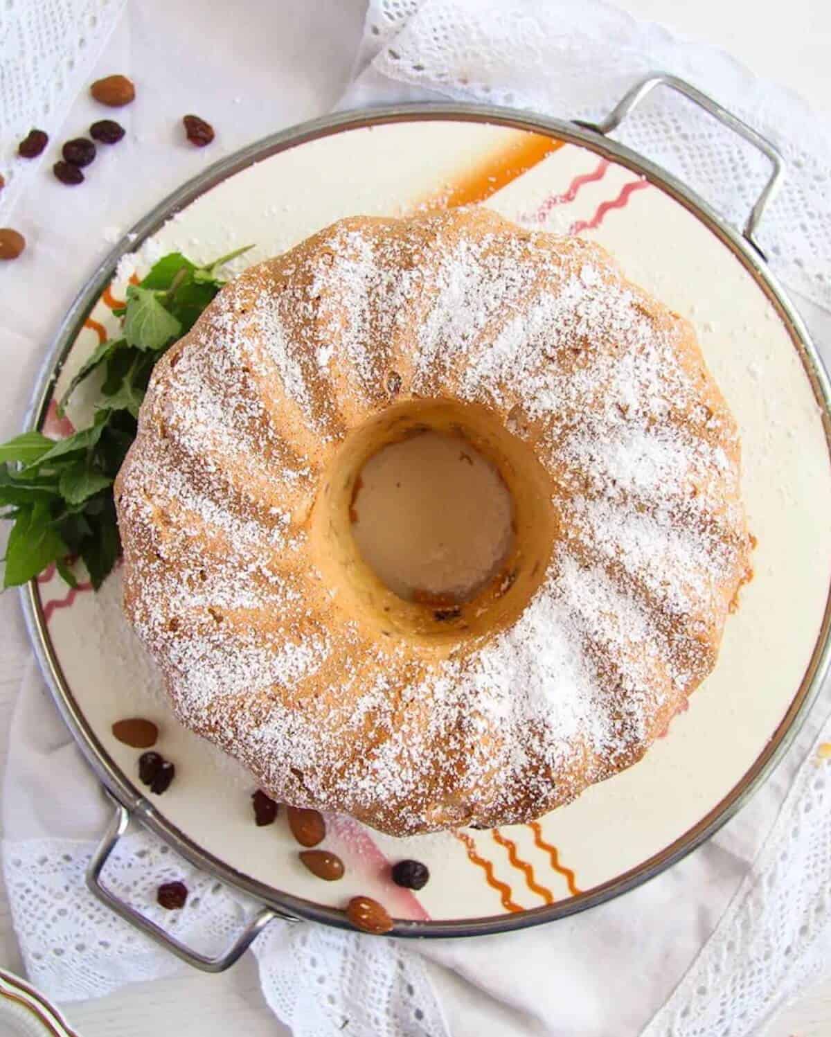 An almond bundt cake on a cake stand, dusted with icing sugar.