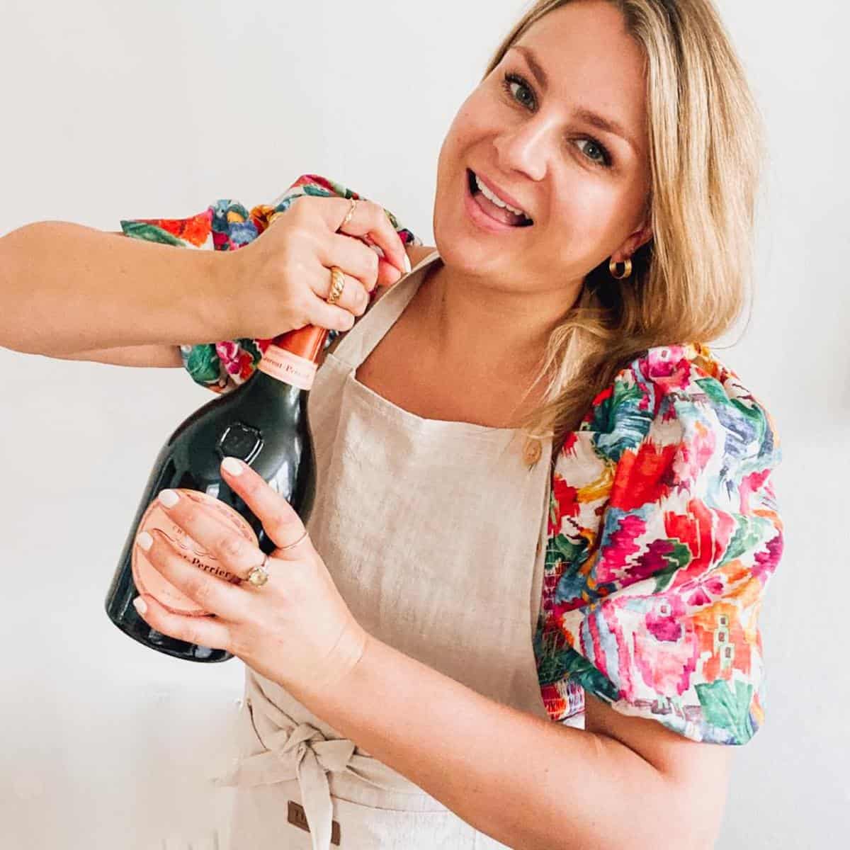 Rosanna Stevens opening a bottle of champagne.