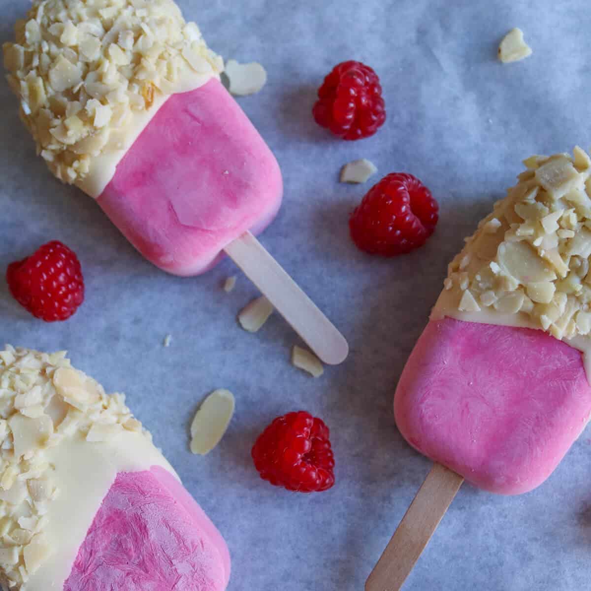 Finished raspberry. white chocolate and almond ice cream bars on a tray surrounded by fresh raspberries. 