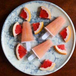 Vodka greyhound ice lollies on a plate with slices of grapefruit