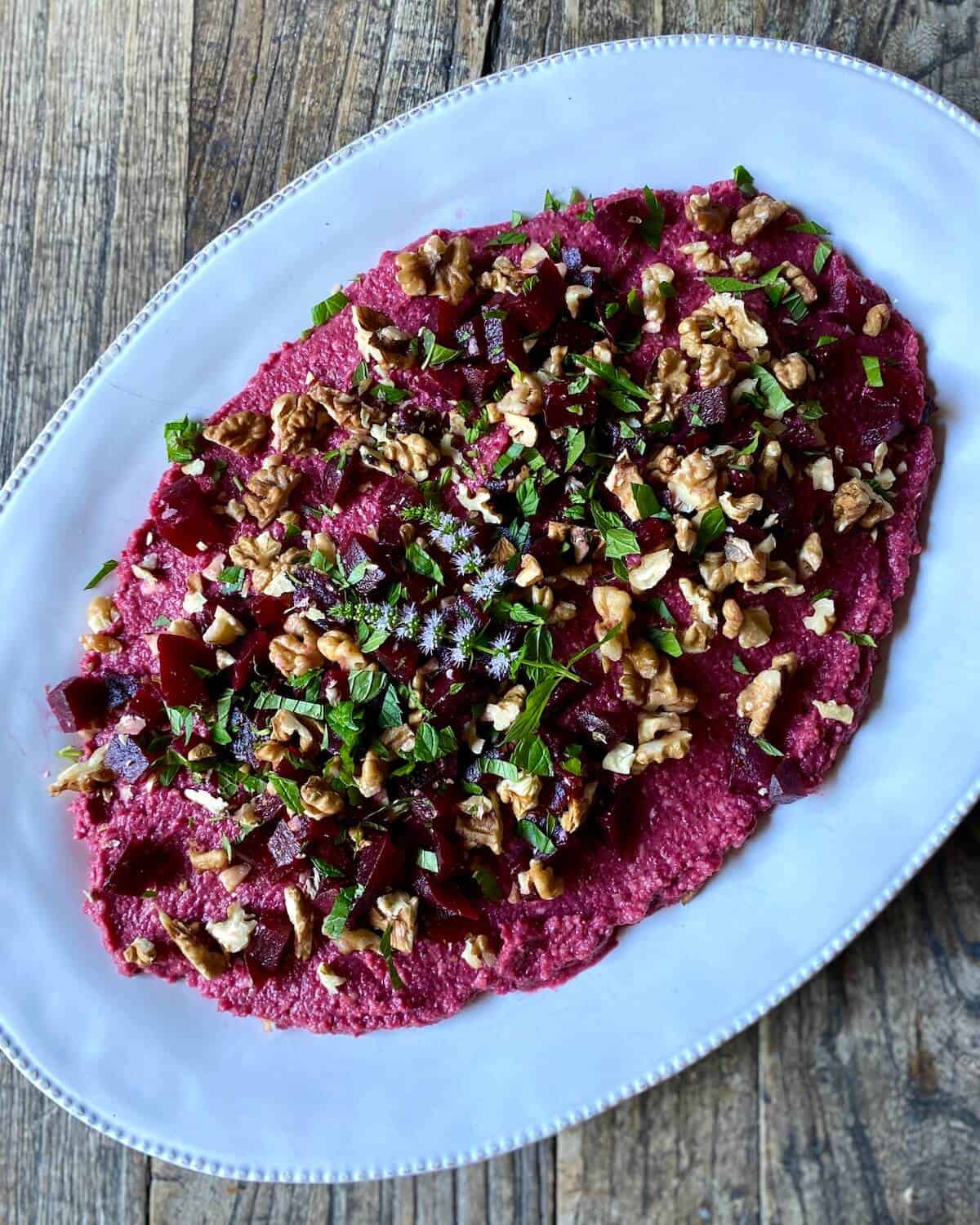 Beetroot hummus on an oval serving platter topped with chopped walnuts and fresh mint.