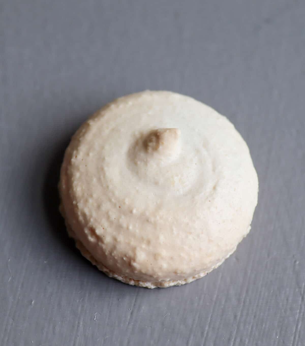 A macaron shell with the piping peak still visible.