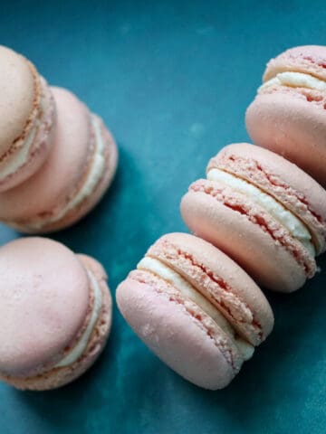 Pink Italian macarons with cream filling on a blue surface.