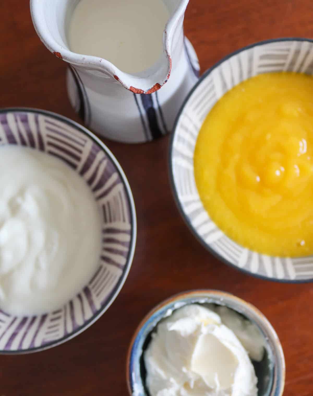 The ingredients for a mango cream filling on a table: double cream, mango coulis, yogurt and mascarpone cheese. 