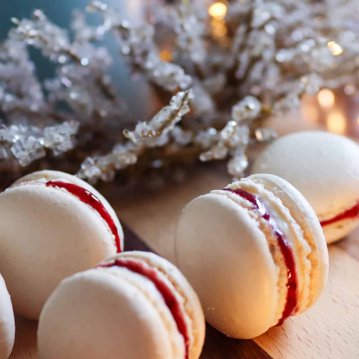 Savoury macarons with a goat cheese and cranberry filling on a wooden chopping board surrounded by fairy lights and a sparkly Christmas wreath. 