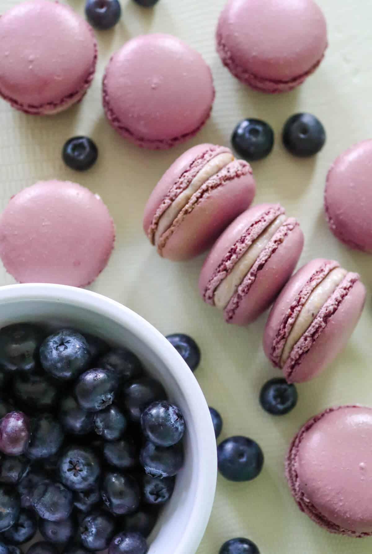 Blueberry cheesecake macarons and fresh blueberries on a table.