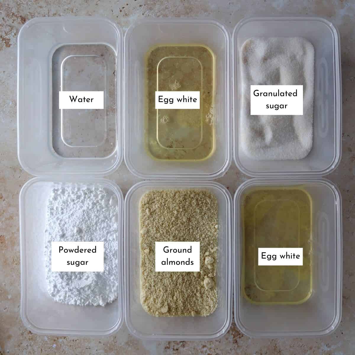 Tupperware containers filled with egg white, powdered sugar, granulated sugar, ground almonds and water.