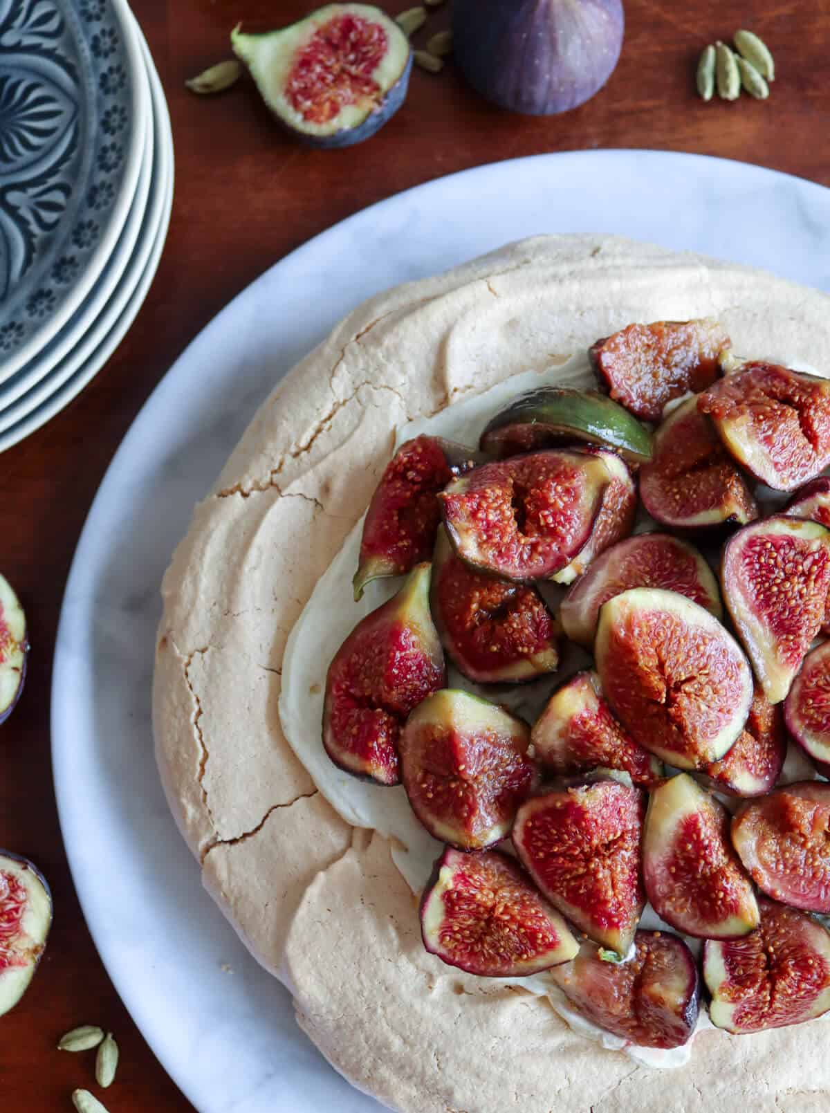 A fig pavlova on a table surrounded by figs and serving plates.