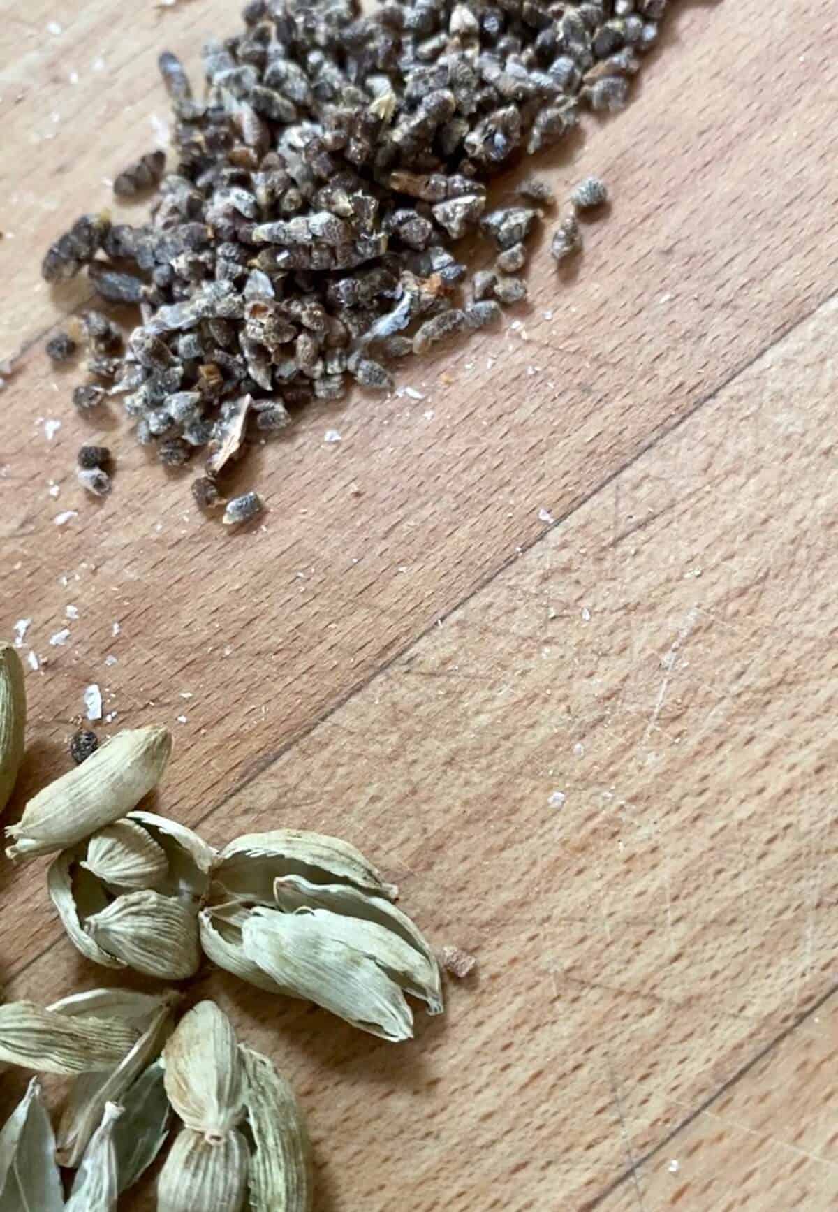 Cardamom pods split open and their seeds in a pile next to them. 