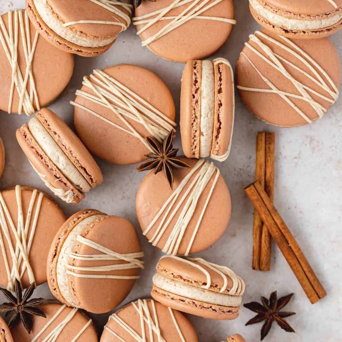 Several chai spice macarons with star anise and cinnamon on a surface.