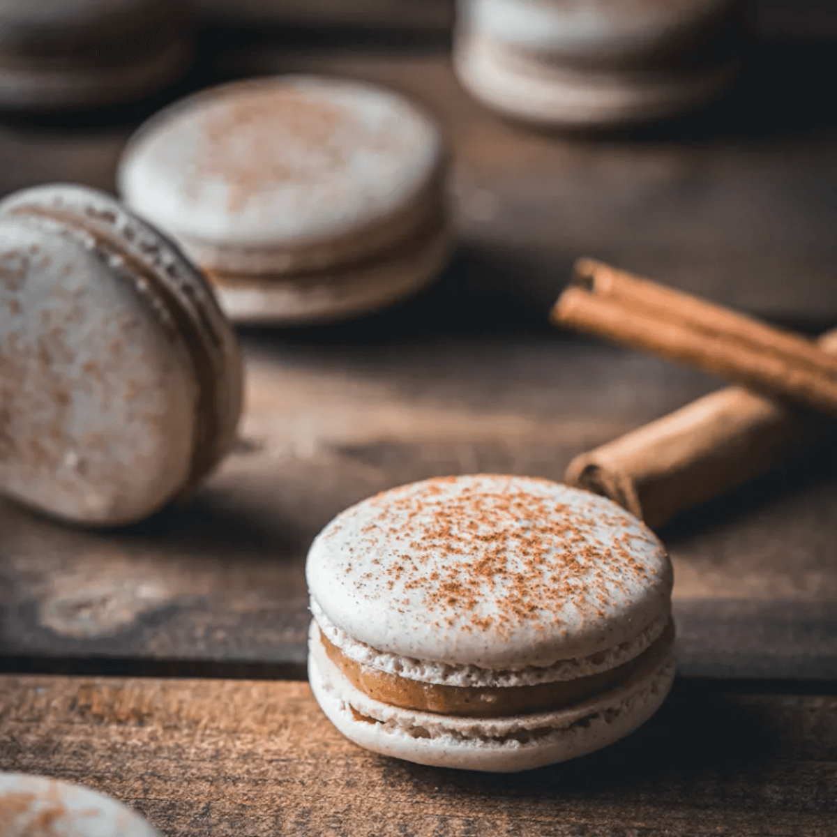 Snickerdoodle macarons on a table with cinnamon sticks.
