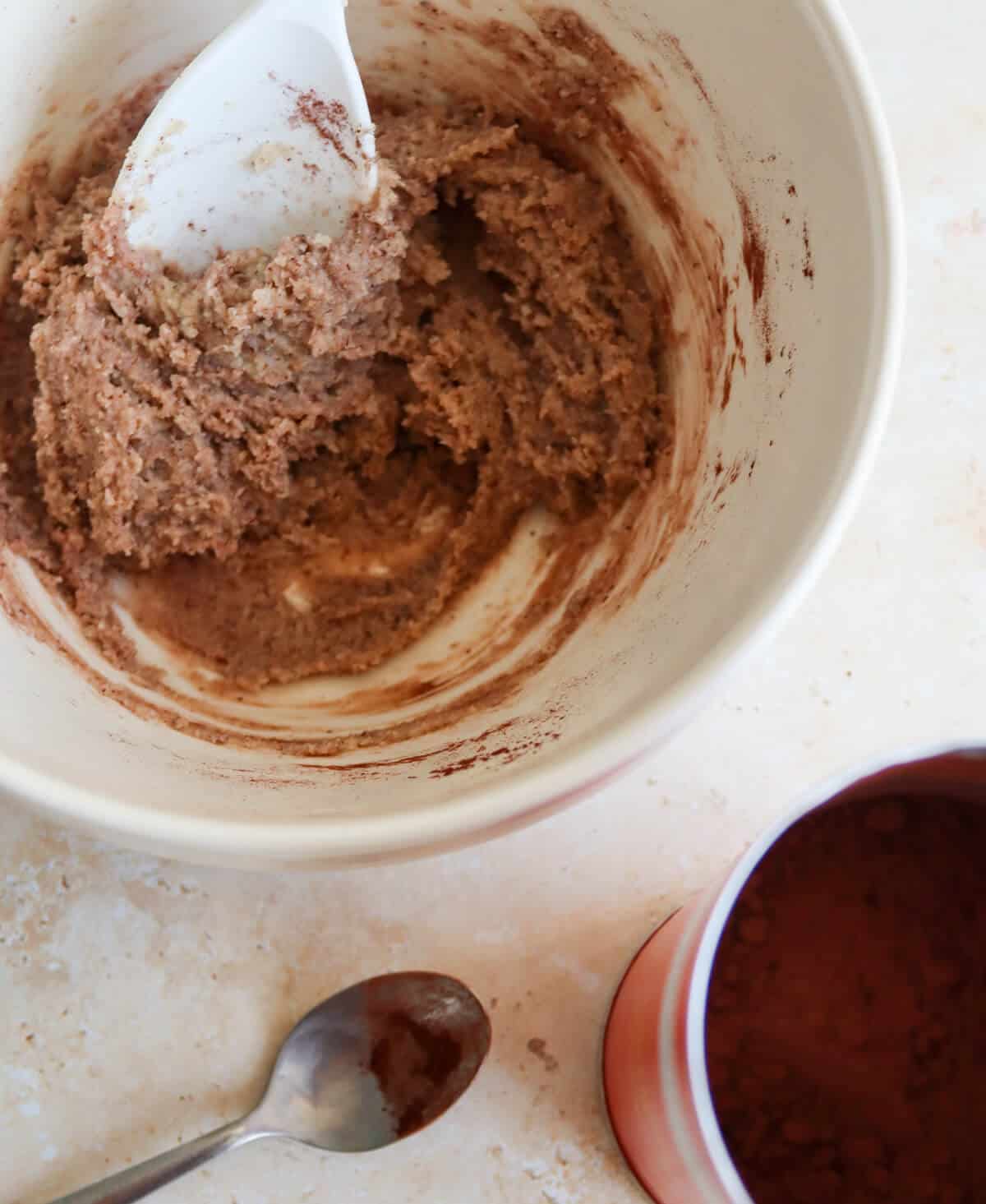 Almond and hazelnut paste in a bowl next to a pot of cocoa powder.