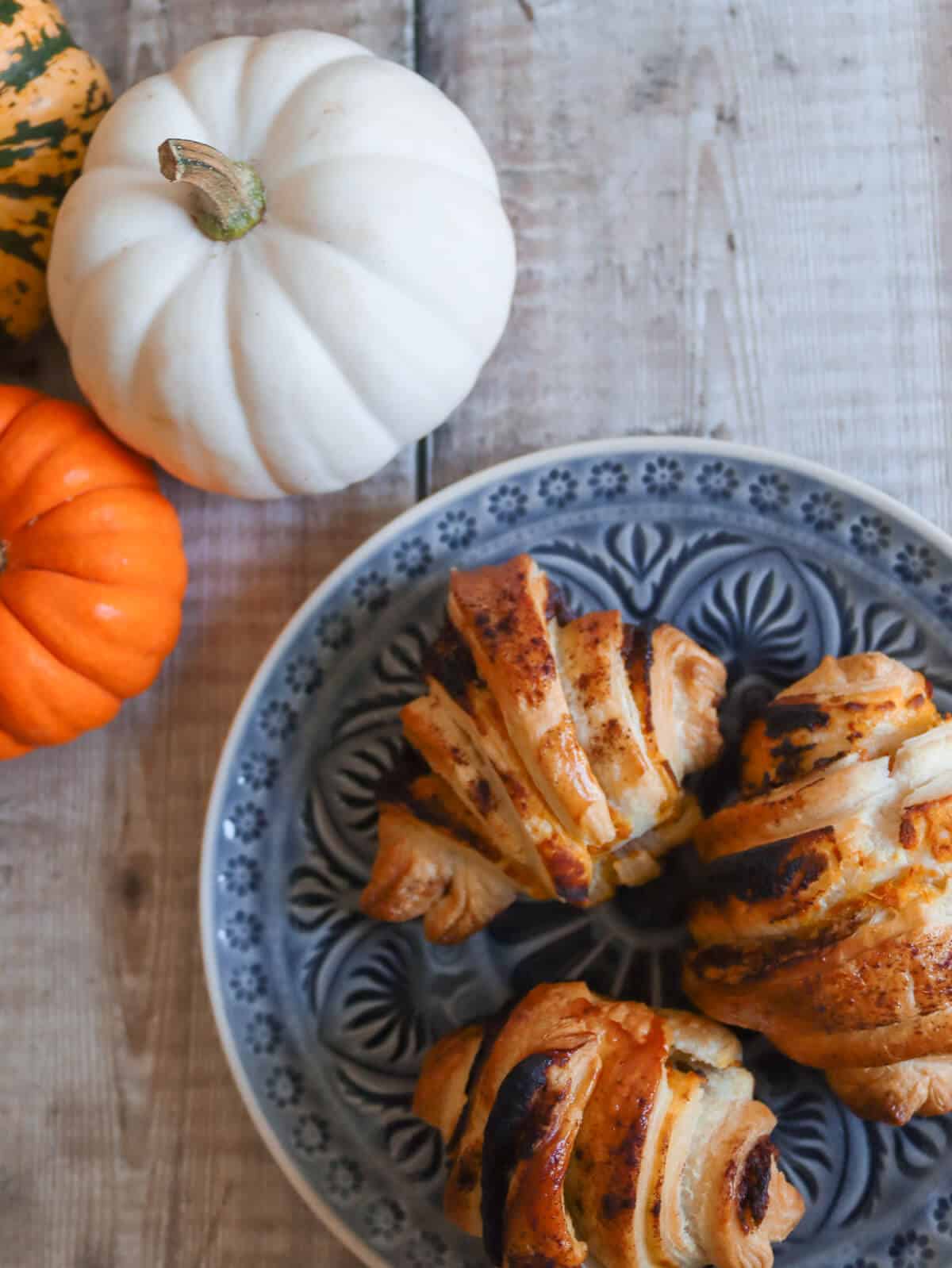 Pumpkin croissants on a plate on a table with decorative pumpkins. 