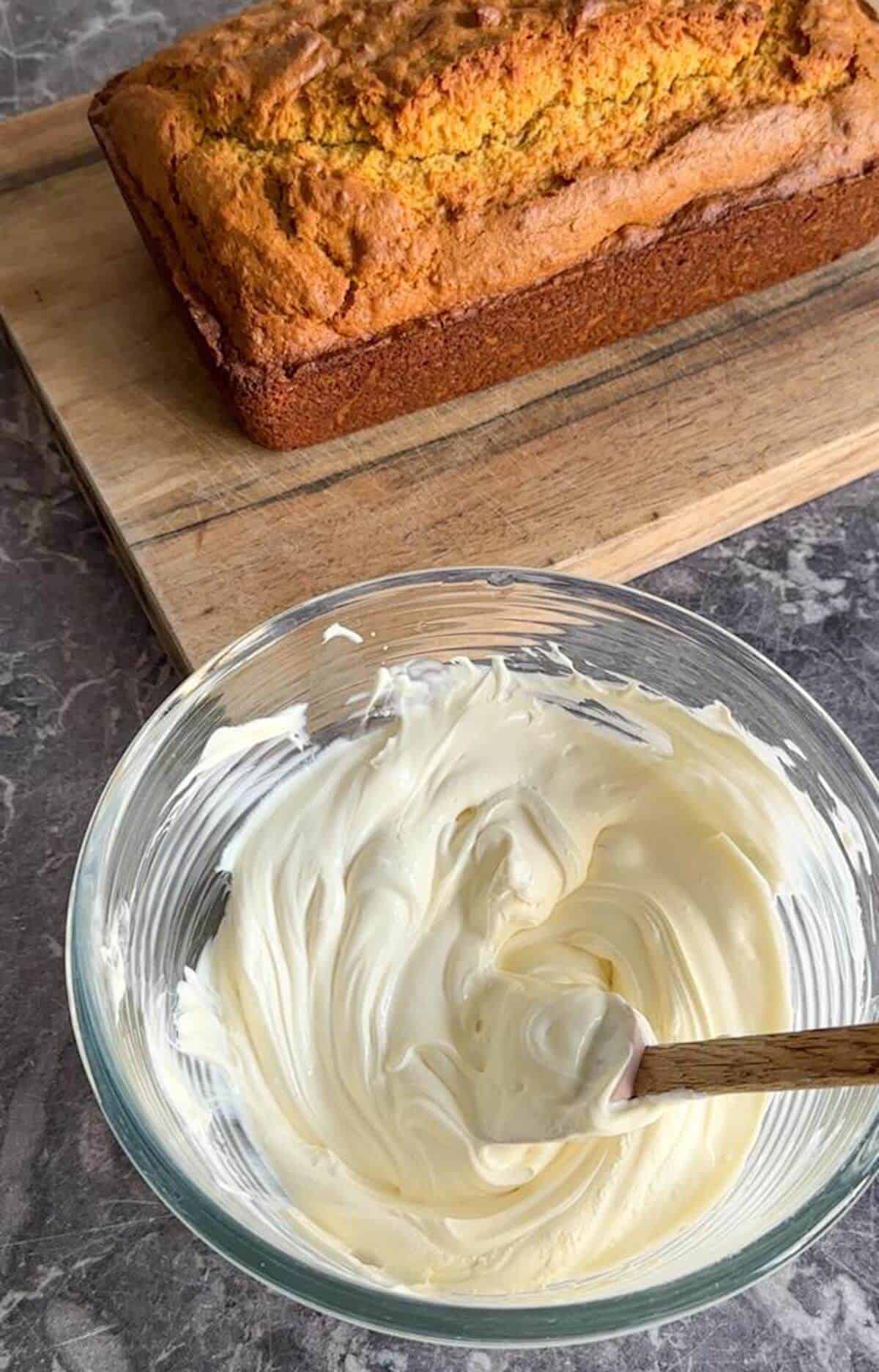 A bowl of mascarpone cream cheese frosting next to a pumpkin loaf cake. 