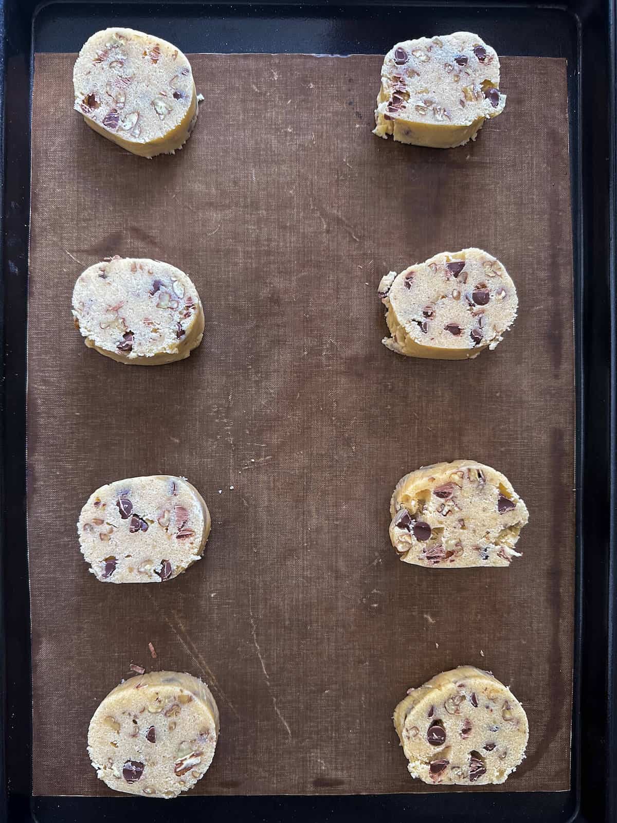 8 slices of cookie dough on a baking sheet.