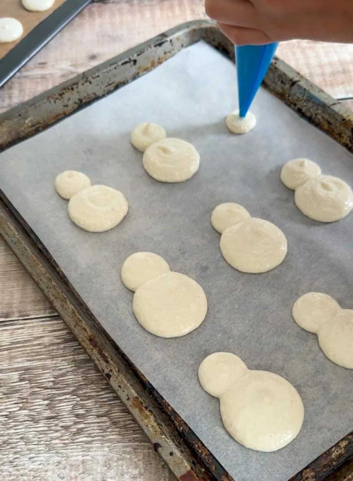 Piping snowman shaped macarons onto a baking tray.