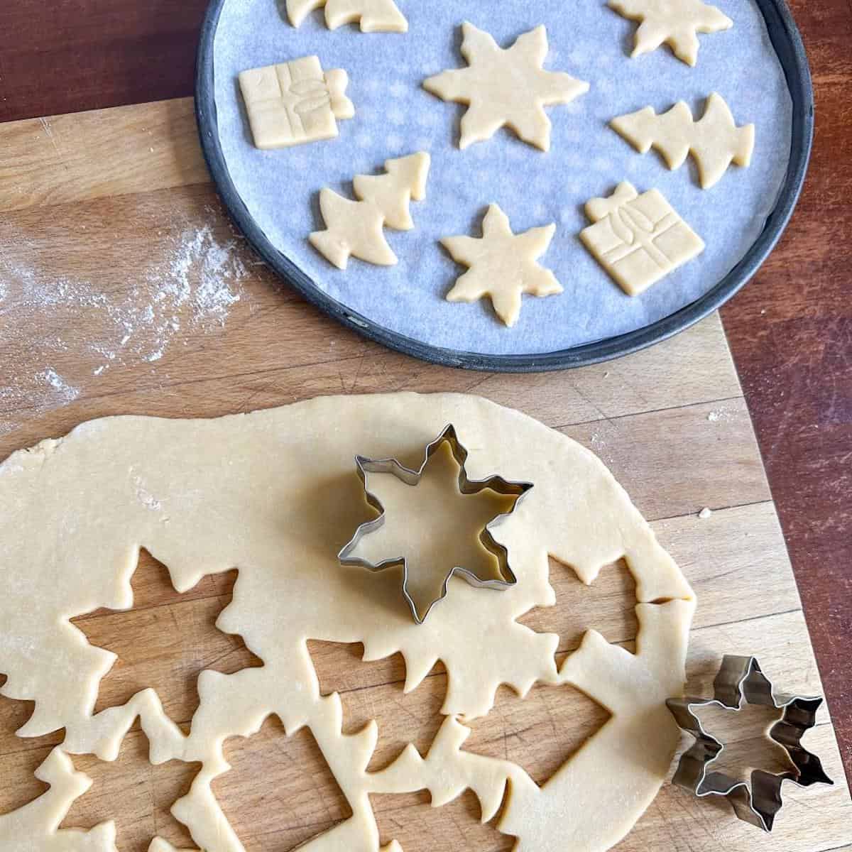 Sweet shortcrust pastry rolled out on a kitchen surface, with cookie cutters and a tray of cookies ready to be baked. 