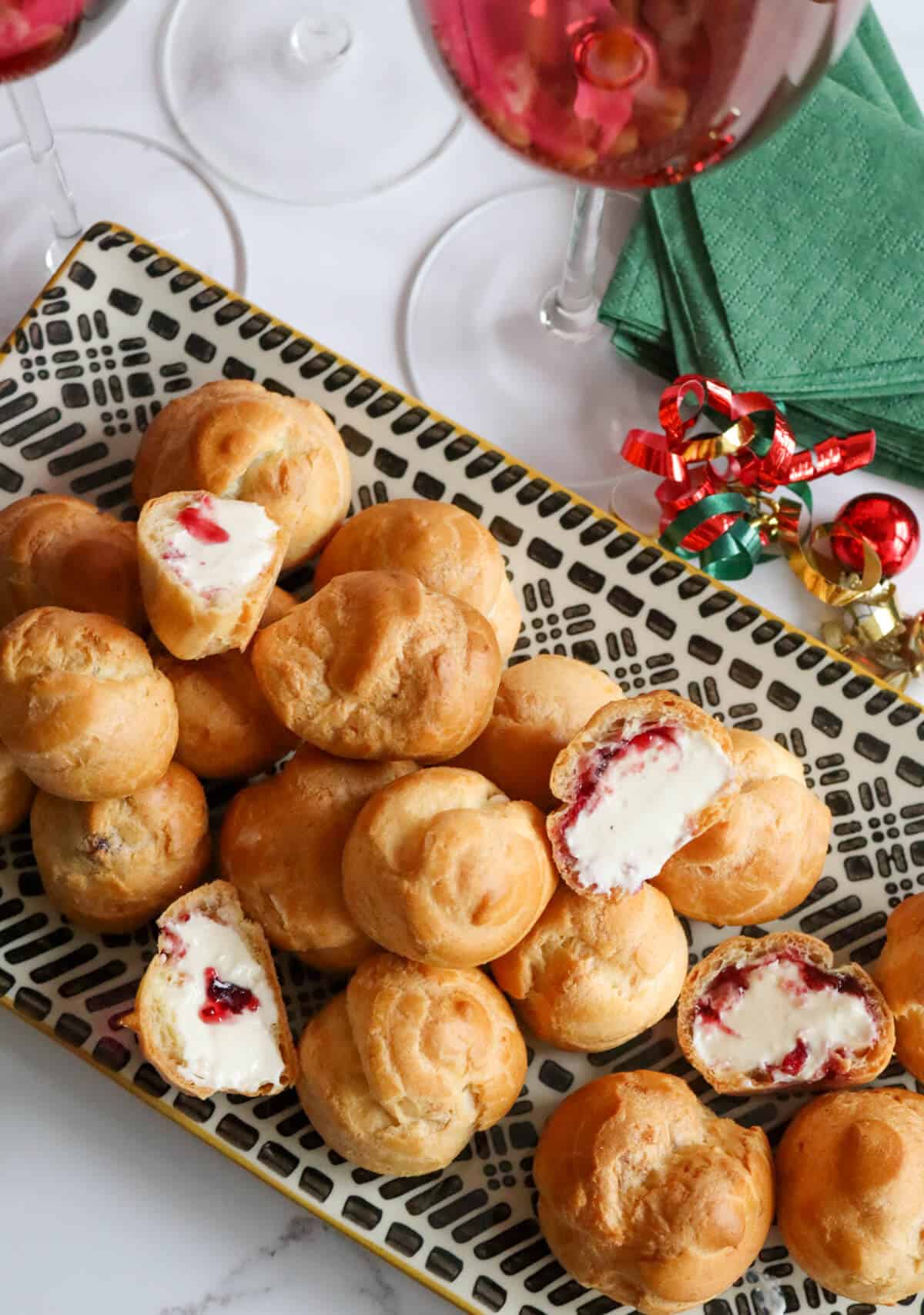 A platter of whipped brie and cranberry profiteroles with wine glasses, napkins and Christmas decorations around it. 