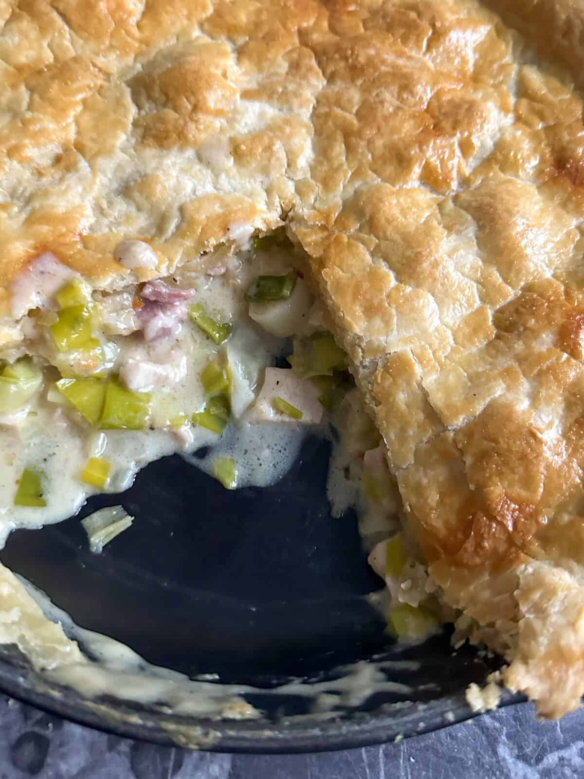 A close up photo of the inside of a slice of turkey and ham pot pie, showing the creamy filling and pastry topping. 