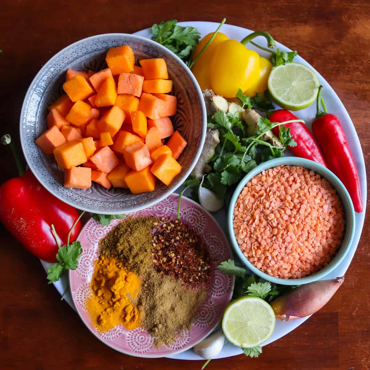 The ingredients for sweet potato dahl on a large plate. Sweet potato and squash, red lentils, coriander, chilli, bell pepper, shallot, garlic, ginger, cumin, turmeric, garam masala and ginger.