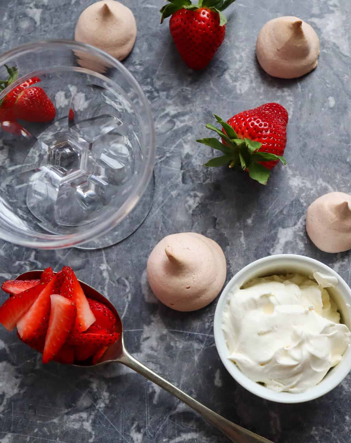 Strawberries, heavy cream and meringue cookies on a table surface. 